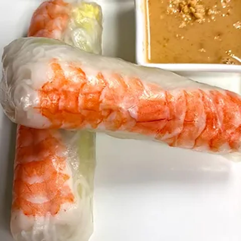 Two fresh shrimp spring rolls with a side of peanut dipping sauce on a white plate.