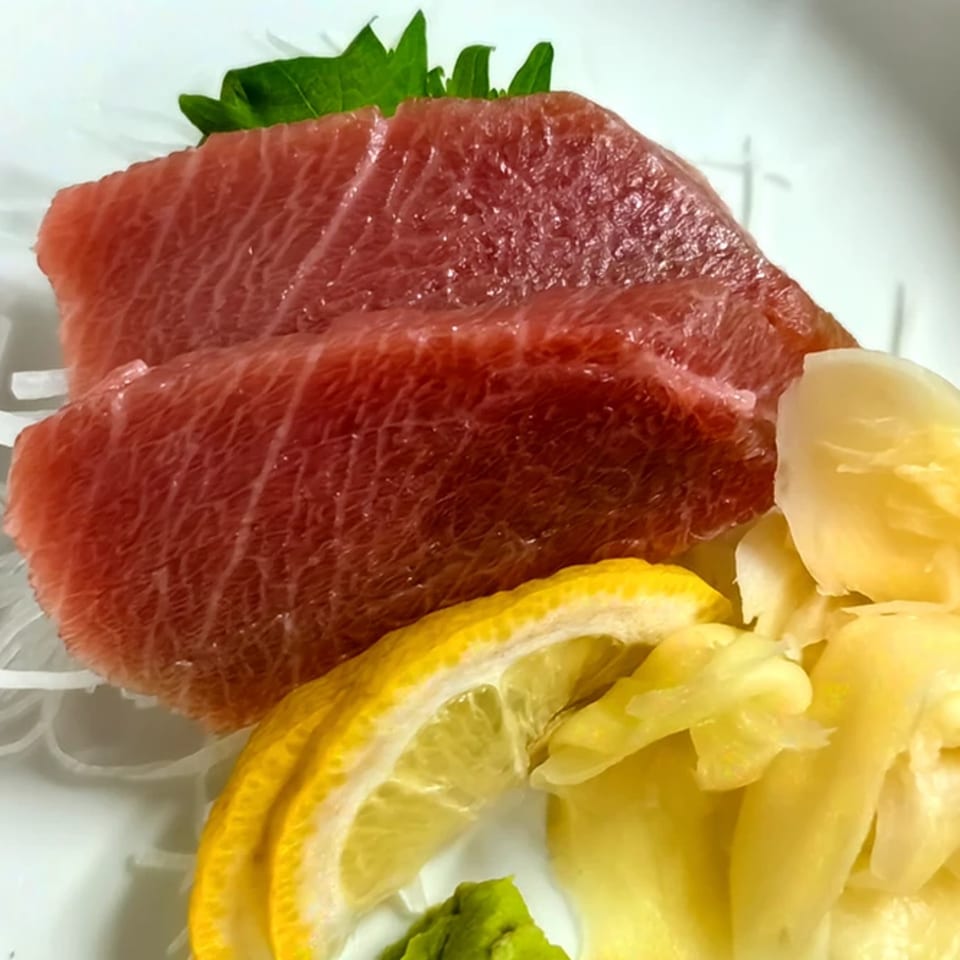 Close-up of Ito Sushi Asian Bistro's tuna sashimi with lemon, pickled ginger, and wasabi.