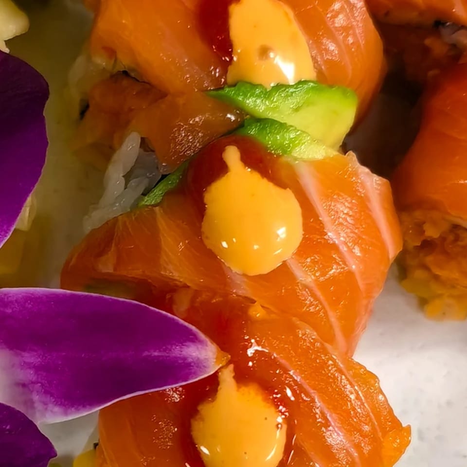 Close-up of Ito Sushi Asian Bistro's salmon sushi rolls with avocado, sauces, and purple orchid petals.
