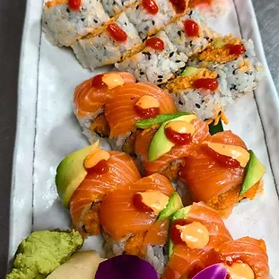 A white platter holds two rows of sushi rolls, one with salmon and avocado, the other with red sauce.