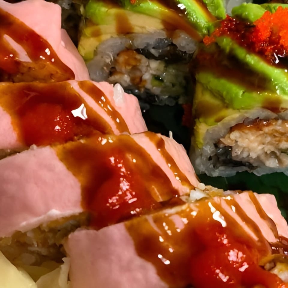 Close-up of Ito Sushi's pink-wrapped sushi rolls drizzled with sauce, alongside avocado and roe-topped rolls.